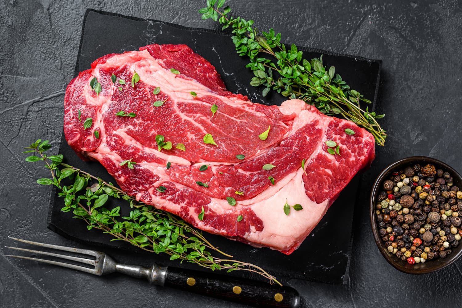 Corte Ribeye natural de Cortes Celorio con hierbas frescas y granos de pimienta, carne premium mexicana lista para parrilla gourmet.